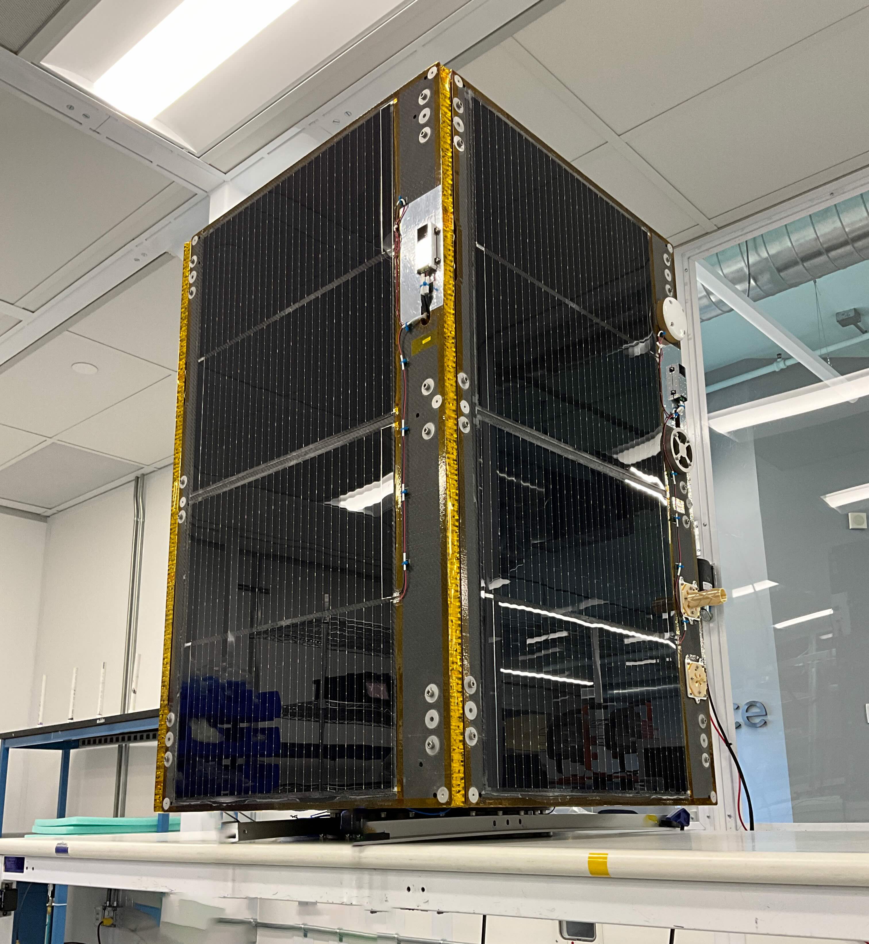 Muon Space's small satellite with body-mounted solar panels sits on a workbench in a cleanroom before its first launch.