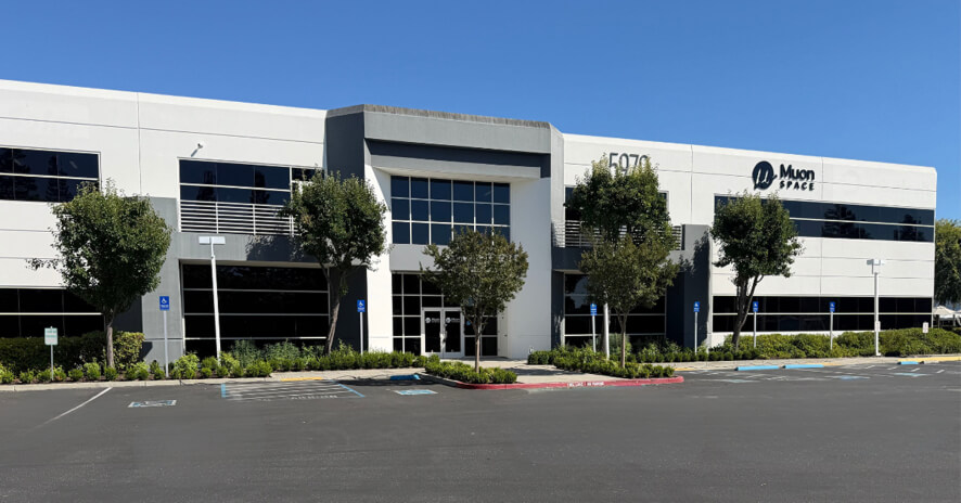 Muon Space headquarters building with company logo, featuring a modern two-story facade, landscaped trees, and a parking lot.