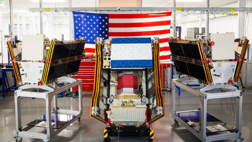 Satellites under assembly on metal carts inside Muon Space's San Jose manufacturing facility, with a large American flag
